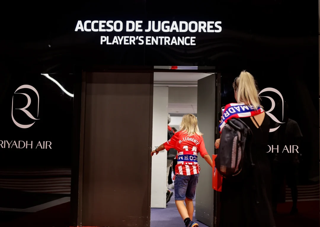 Child wearing football T-shirt and followed by parents walks through doors into Player's Entrance of Atletico de Madrid stadium.